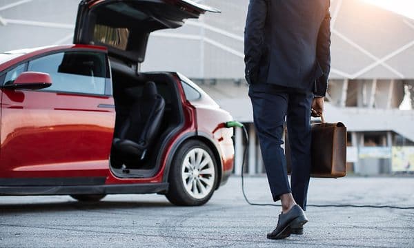  Man med portfölj som går mot en öppen röd Tesla