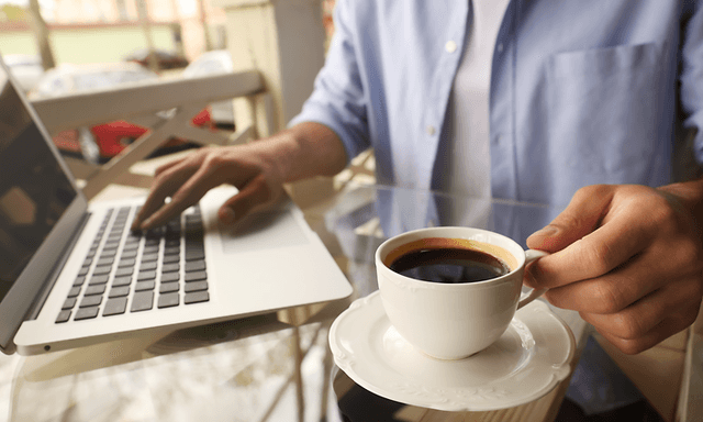 person sitter med en full kaffekopp og jobber på en bærbar pc
