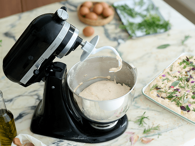 En Kitchenaid kjøkkenmaskin med en bolle full av deig og en foccacia med blomster som er klar til å stekes